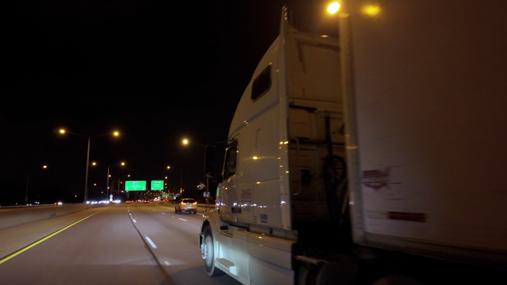 Wide-angle view of a semi-truck driving on a U.S. highway at night