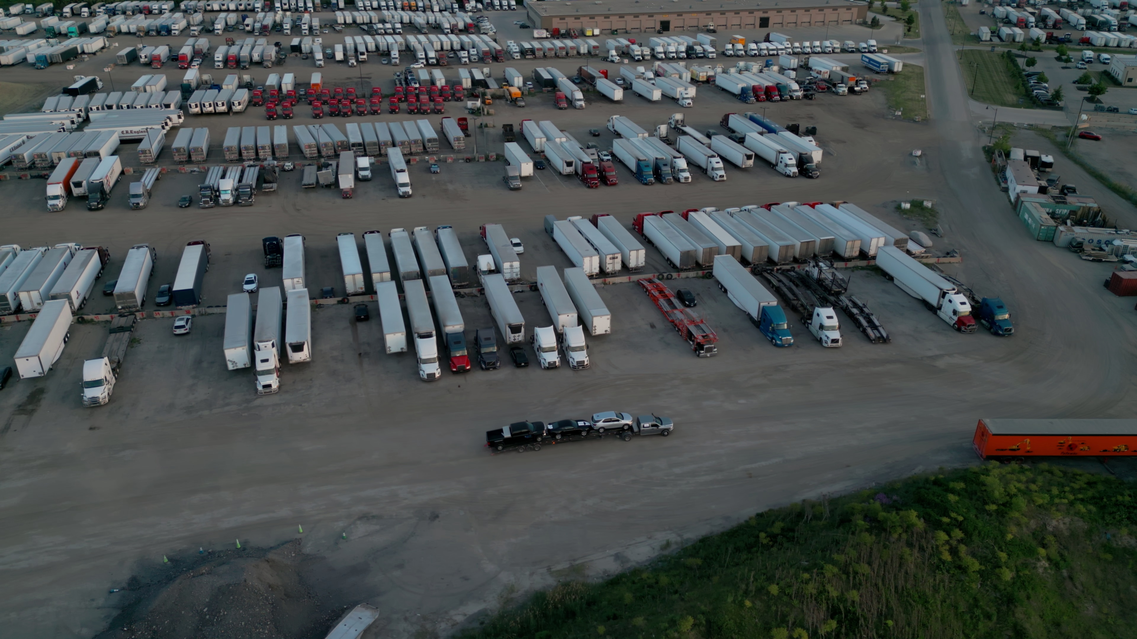 Aerial wide shot of a semi-truck exiting a U.S. truck stop parking lot in spring 2026